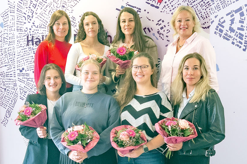Mehrere Frauen lächeln in die Kamera, 6 von ihnen halten einen Blumenstrauß in der Hand.