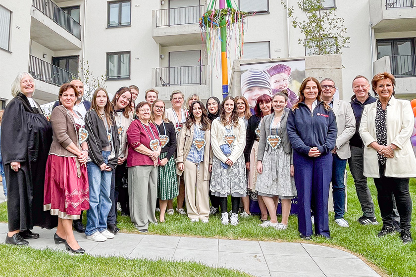 Mehrere Leute stehen vor einem bunten Maibaum, einige haben ein Lebkuchenherz um.