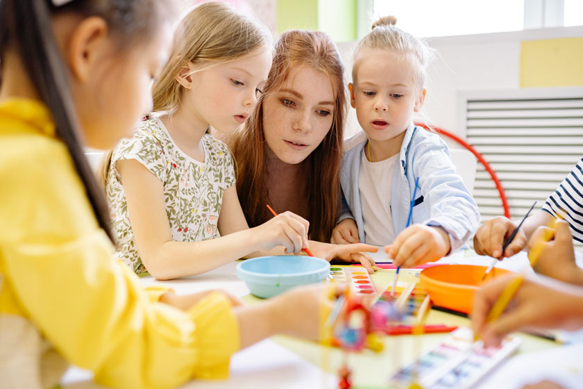 Eine pädagogische Fachkraft spielt mit 3 Kindern in einer Kita.