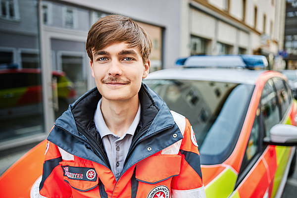 Ein junger Mitarbeiter steht vor dem Hausnotrufauto