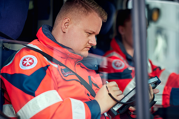 Ein Mitarbeiter des Rettungsdienstes sitzt mit einer Kollegin im Rettungswagen und protokolliert etwas.