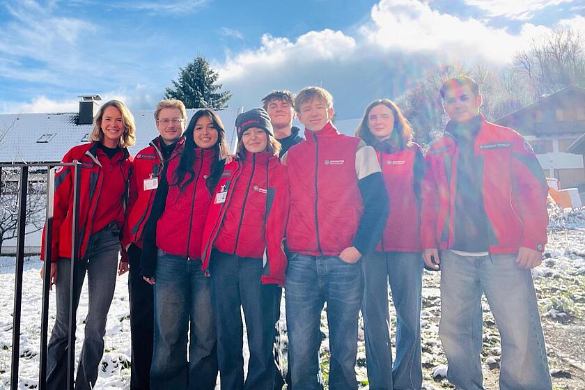Mehrere junge Leute in Johanniter Kleidung stehen auf einer zugeschneiten Wiese.