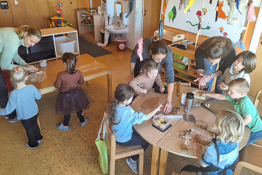 Mehrere Kinder backen zusammen mit Erzieherinnen Plätzchen.