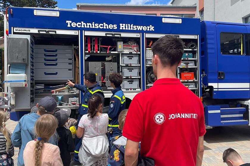 Das Bild zeigt ein Einsatzfahrzeug des THWs mit Kindern, die begeistert das Auto besichtigen.