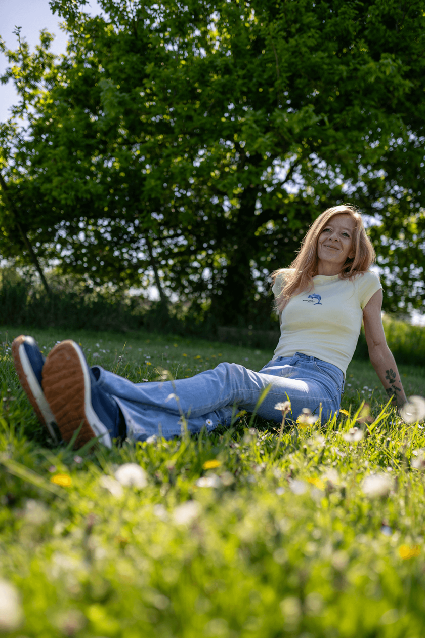 Frau sitzt entspannt auf einer Wiese, lächelt in die Sonne.  