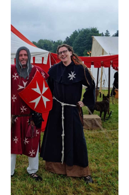 Frau in historischer Gewandung aus dem Mittelalter steht auf einer Wiese.