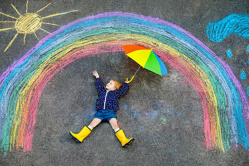 Kind mit Schirm unter einem gemalten Regenbogen