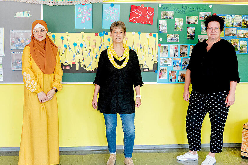 3 Frauen stehen vor einer Wand mit von Kindern gebastelten Bildern.