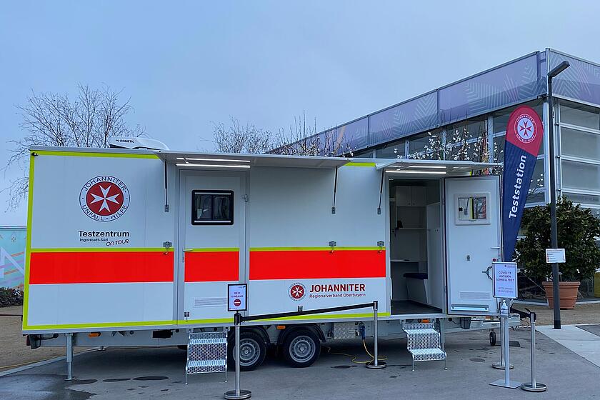 Ein Johanniter Testzentrum mit der Aufschrift "Testzentrum Ingolstadt-Süd on-tour" steht vor einem Geschäft