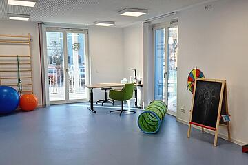 Bild vom Bewegungsraum der Praxis mit Klettersprossen, Bällen, Kriechtunnel und anderen Spielgeräten