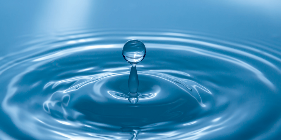Ein Tropfen fällt auf eine Wasseroberfläche. Das ganze Bild ist blaugefärbt.