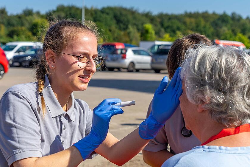 Eine Sanitätshelferin leuchtet einer Patientin in die Augen, um ihren Bewusstseinszustand zu überprüfen.