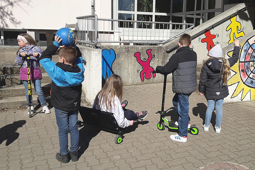 Kinder beim Rollerfahren im Schulhof