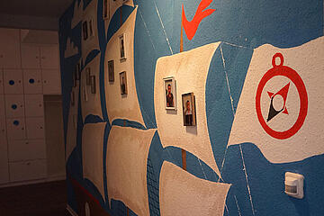 Bemalte Wand mit Segelschiffen und dem Kompass-Logo