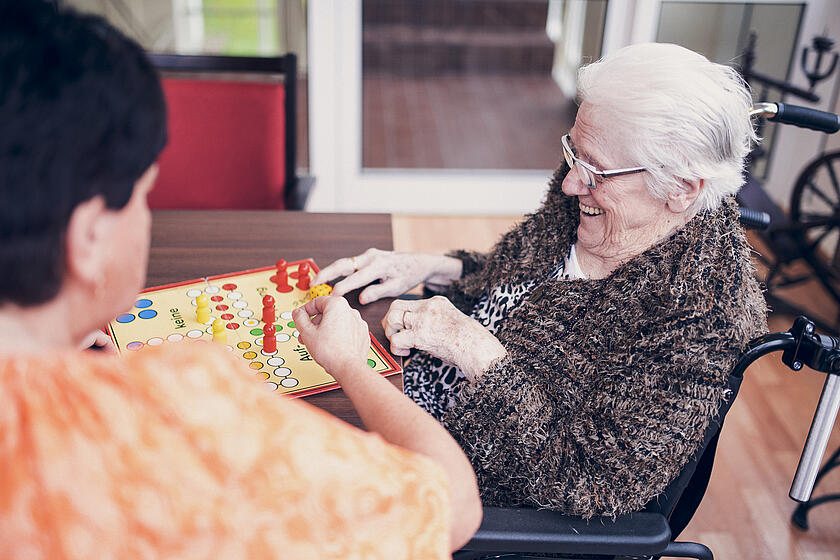 Eine Bewohnerin und eine Mitarbeiterin spielen zusammen ein Brettspiel
