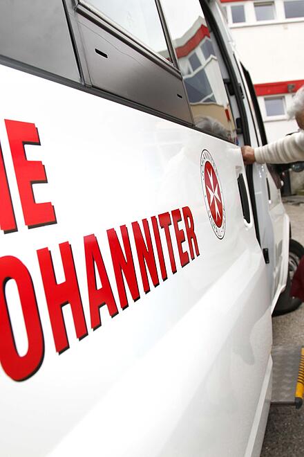 Ein Mitarbeiter des Fahrdiensts der Johanniter-Unfall-Hilfe hilft einer älteren Frau beim Einsteigen in ein Auto.