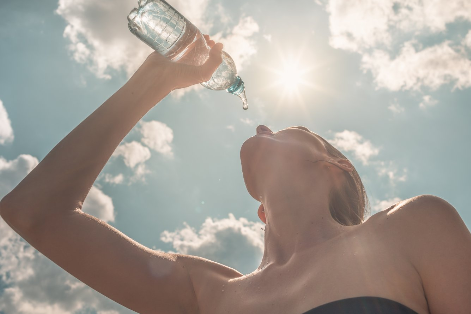 Eine Frau trinkt aus einer Wasserflache. Sie ist von unten gegen den Himmel fotografiert.
