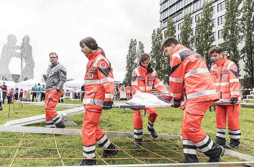 Vier Jugendliche tragen eine Trage durch den Parkour