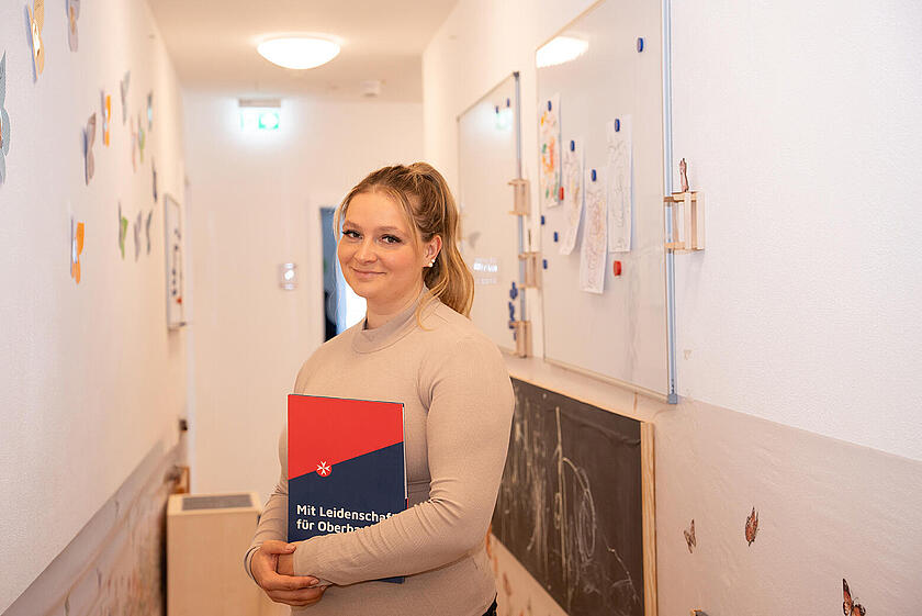 Ein Portrait von Kathrin Haake wie sie im Flur einer Kita steht und eine Johanniter-Mappe in der Hand hält.