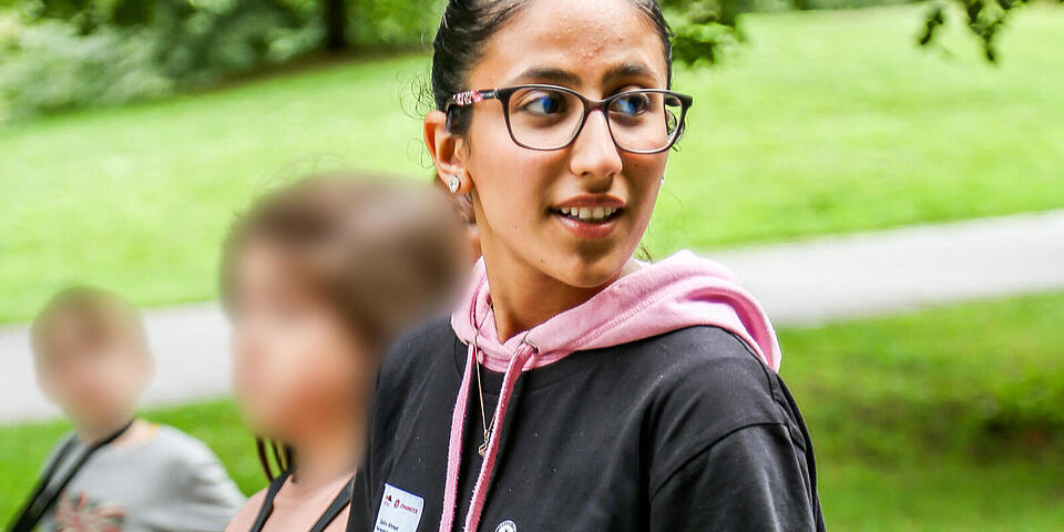 Ferienbetreuung im Freien: Betreuerin führt Kinder Hand in Hand über den Weg.