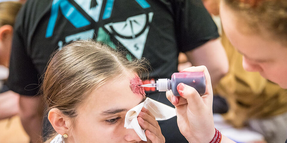Jugendliche wird mit einer realistischen Kopfverletzung geschminkt