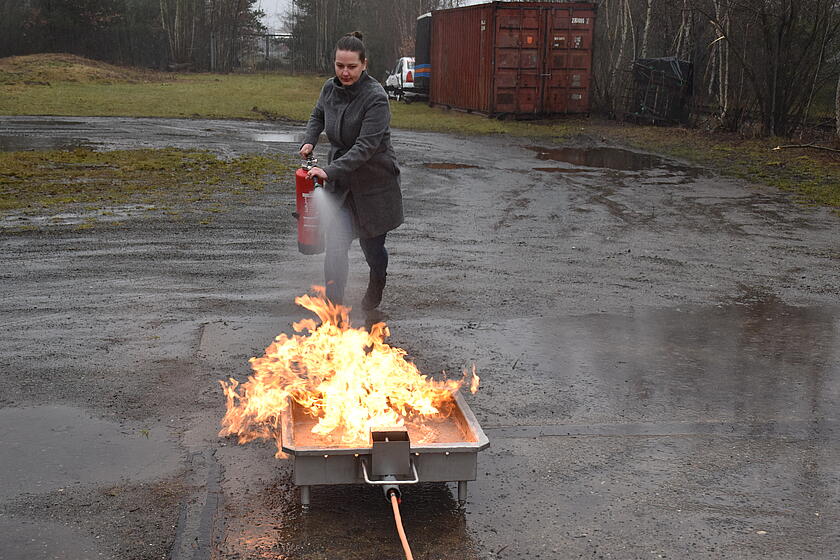 eine Helferin löscht mit dem Feuerlöscher ein kleines Feuer