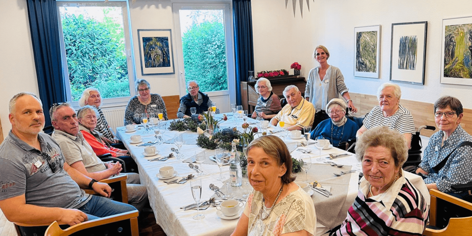 14 Personen um einen großen Tisch, alle blicken zur Kamera