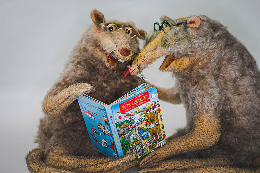 Zwei Leseratten-Kuscheltiere blicken in ein Johanniter Wimmelbuch.
