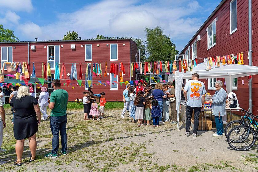 Viele Menschen stehen auf dem Außengelände der Gemeinschaftsunterkunft und vor einem Stand mit einer Tombola.