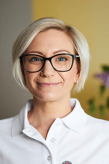 Eine Frau mit Brille steht vor einer gelben Wand