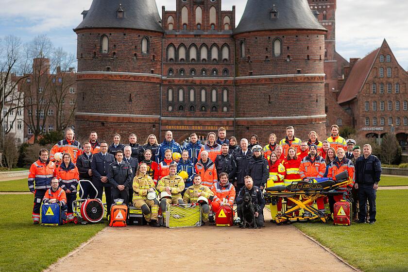 Eine Gruppe von Einsatzkräften der Hilfsorganisationen, Polizei, Feuerwehr und THW steht vor dem Holstentor in Lübeck.