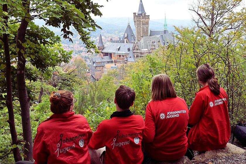 Vier Mitglieder der Johanniter-Jugend sitzen auf einem Felsen und blicken auf eine Stadt
