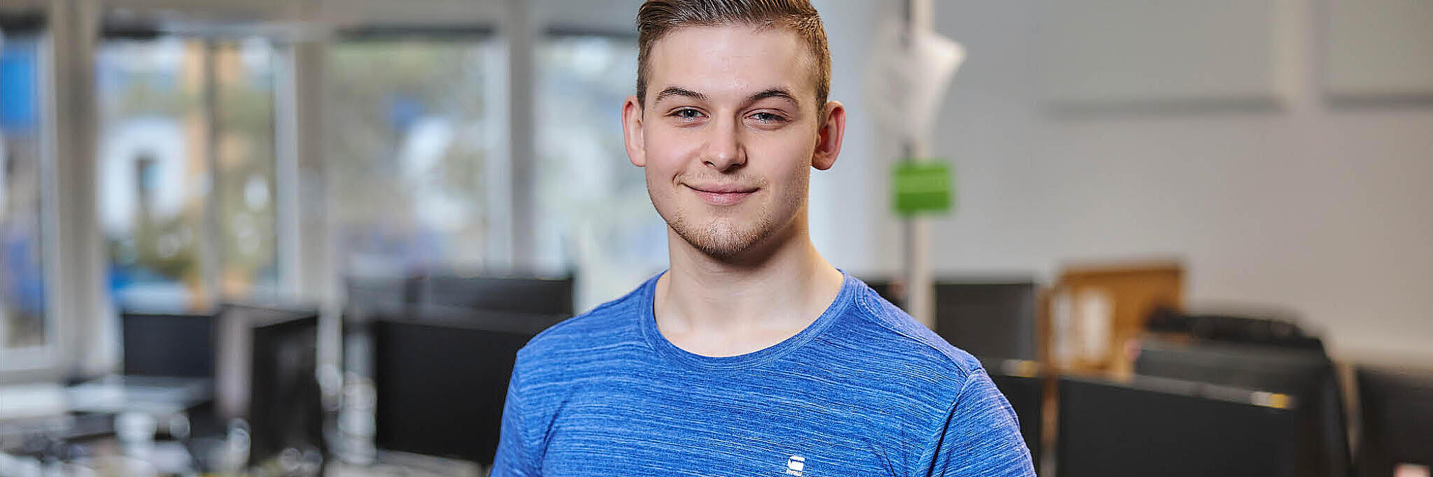 Ein junger Mann steht in einem Büro und lacht in die Kamera