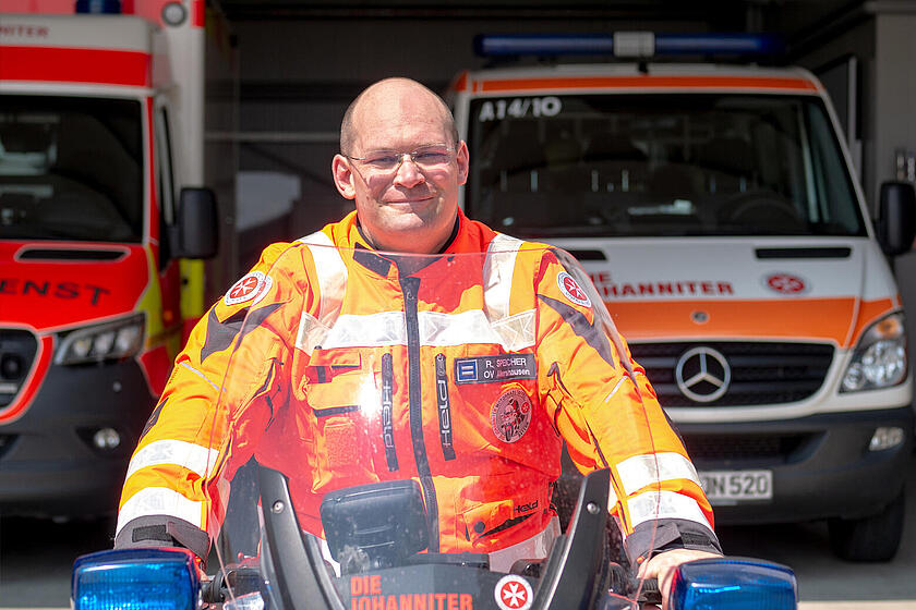 Ein Johanniter in Einsatzkleidung sitzt auf einem Motorrad.