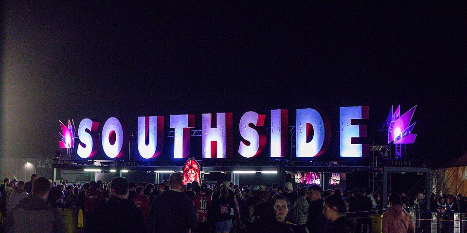 Große leuchtende SOUTHSIDE‑Buchstaben über dem Festivaleingang bei Nacht, davor silhouettenhafte Menschenmenge.