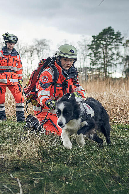 Zwei Einsatzkräfte der Rettungshundestaffel mit einem Rettungshund im Wald