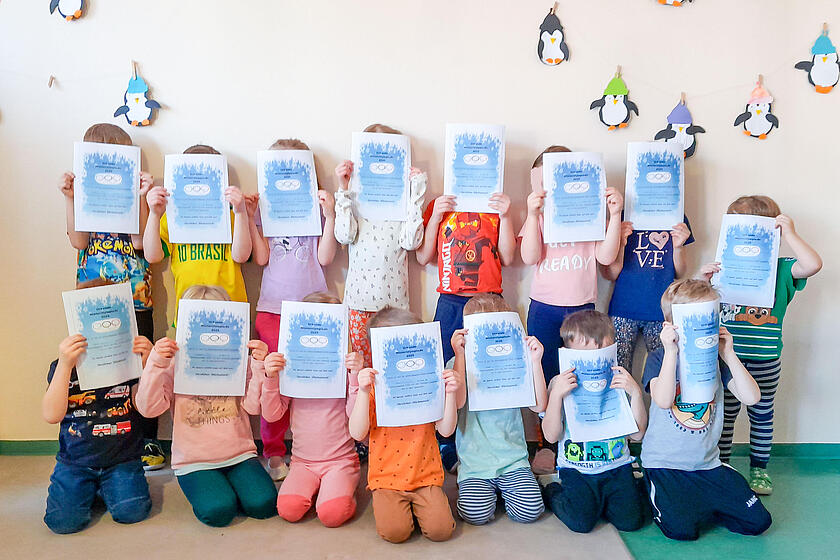 Die Kinder der Kita Gänseblümchen stehen für ein Gruppenfoto zusammen und halten sich die Urkunden vor das Gesicht.