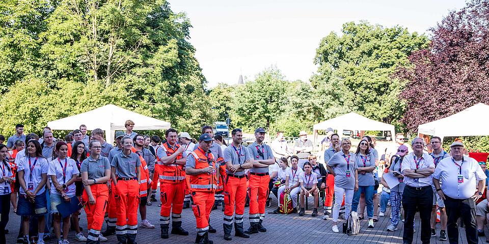  Eine große Gruppe von Einsatzkräften und Helfer*innen im Freien die aufmerksam zuhören