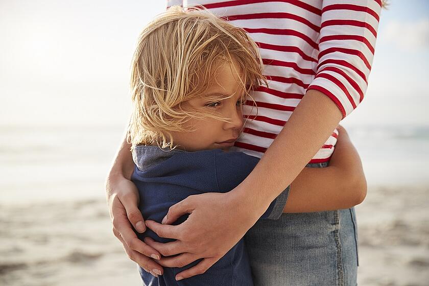 Ein Kind umarmt eine Frau am Strand