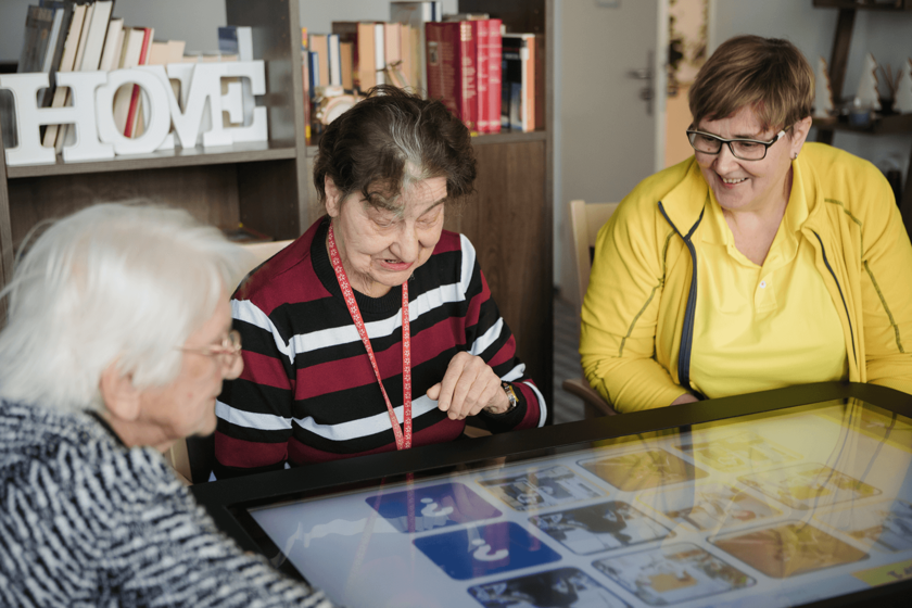 Drei Seniorinnen spielen gemeinsam an einem digitalen Tisch.
