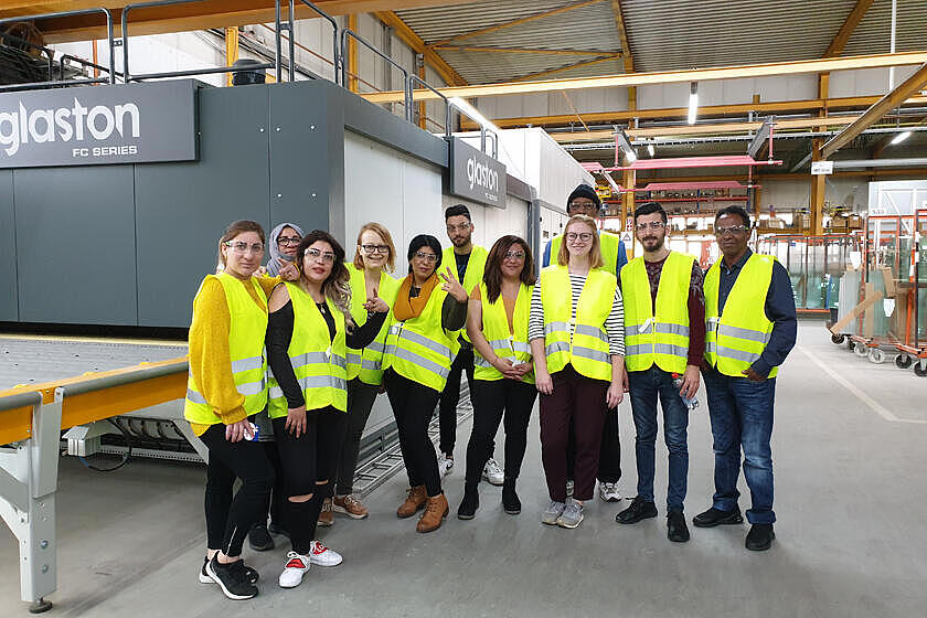 Teilnehmende der Erstorientierungskurse und ihre Lehrkräfte stehen in der Produktionshalle der Interpane Glasindustrie AG. 