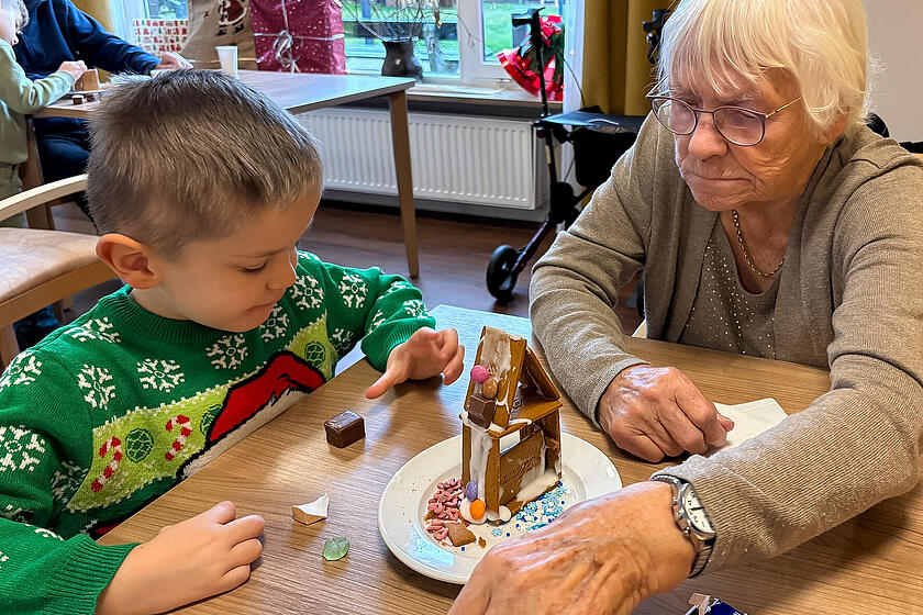 Ein Junge dekoriert gemeinsam mit einer älteren Frau ein Lebkuchenhaus.