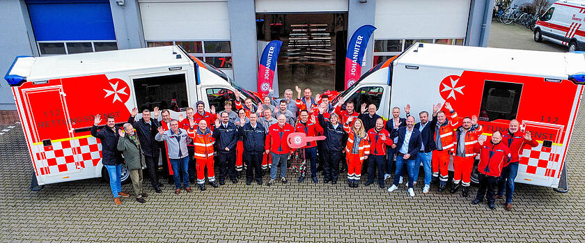 Gruppenbild mehrerer Johanniter aus Drohnenperspektive vor zwei neuen RTW