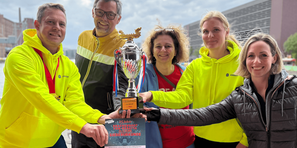 Mehrere Personen halten gemeinsam Pokal und Urkunde lächelnd in die Kamera.
