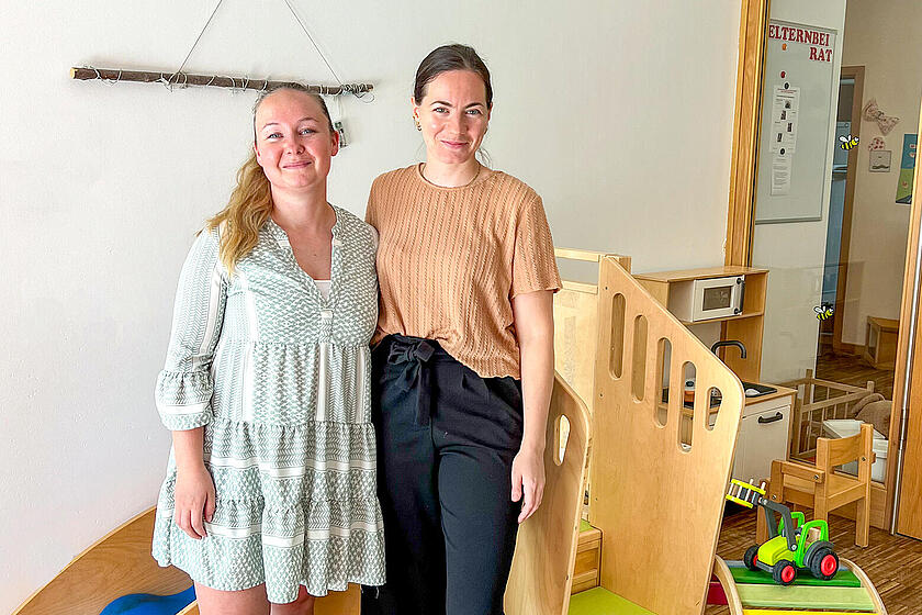 Zwei Frauen stehen vor einer Kinderrutsche und lächeln in die Kamera.