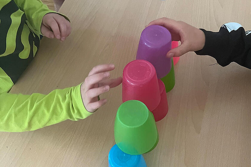 Kinder bauen eine Pyramide aus bunten Plastikbechern.