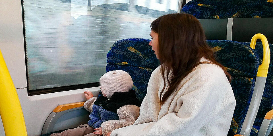 Eine Frau mit einem Kleinkind in einem Linienbus. Das Kind schaut aus dem Fenster.