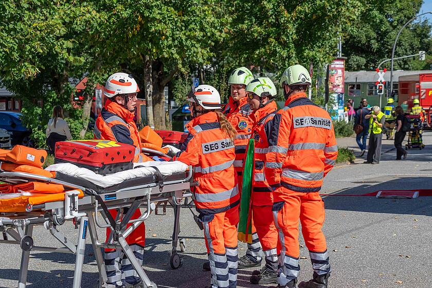 Fünf Ehrenamtliche in Einsatzkleidung stehen an einer Trage und warten auf ihren Einsatz.