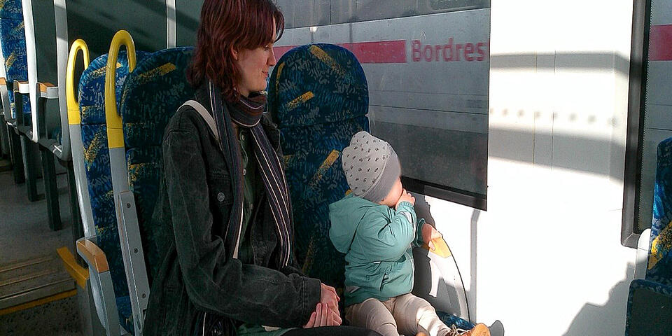 Eine Frau mit einem Kleinkind im Zug. Das Kind schaut aus dem Fenster und sieht einen weiteren Zug