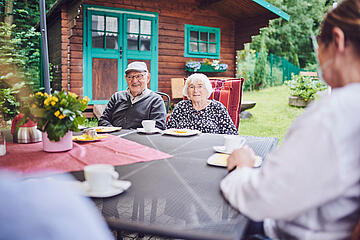 Ein älteres Paar sitzt an einem Tisch im Garten und lächeln